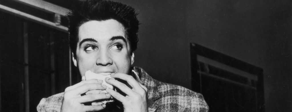 A still-trim Elvis Presley enjoys a sandwich in 1958. His love of fatty foods hadn't caught up to him yet.